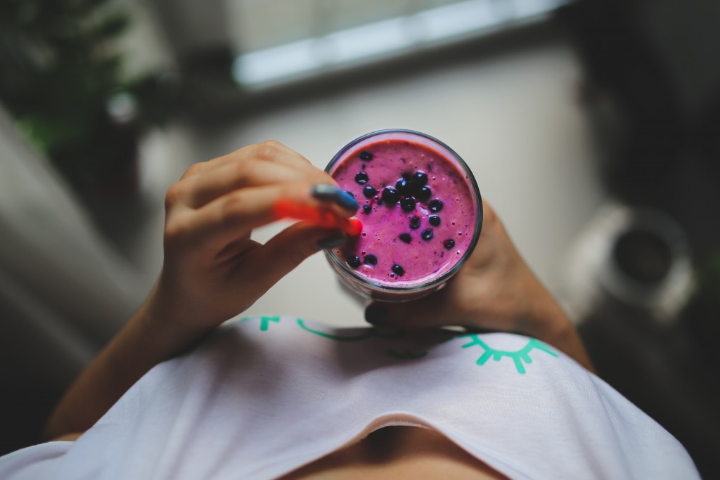 Image of a woman holding a purple berry smoothing symbolising a healthy lifestyle and increase in productivity for employees who have Corporate Health Assessments